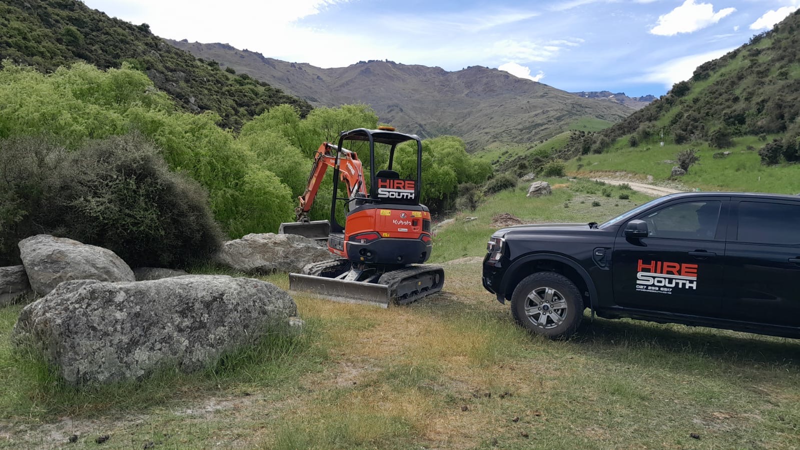 Hire South branded Kubota mini digger and black ute parked in a scenic Central Otago mountain valley