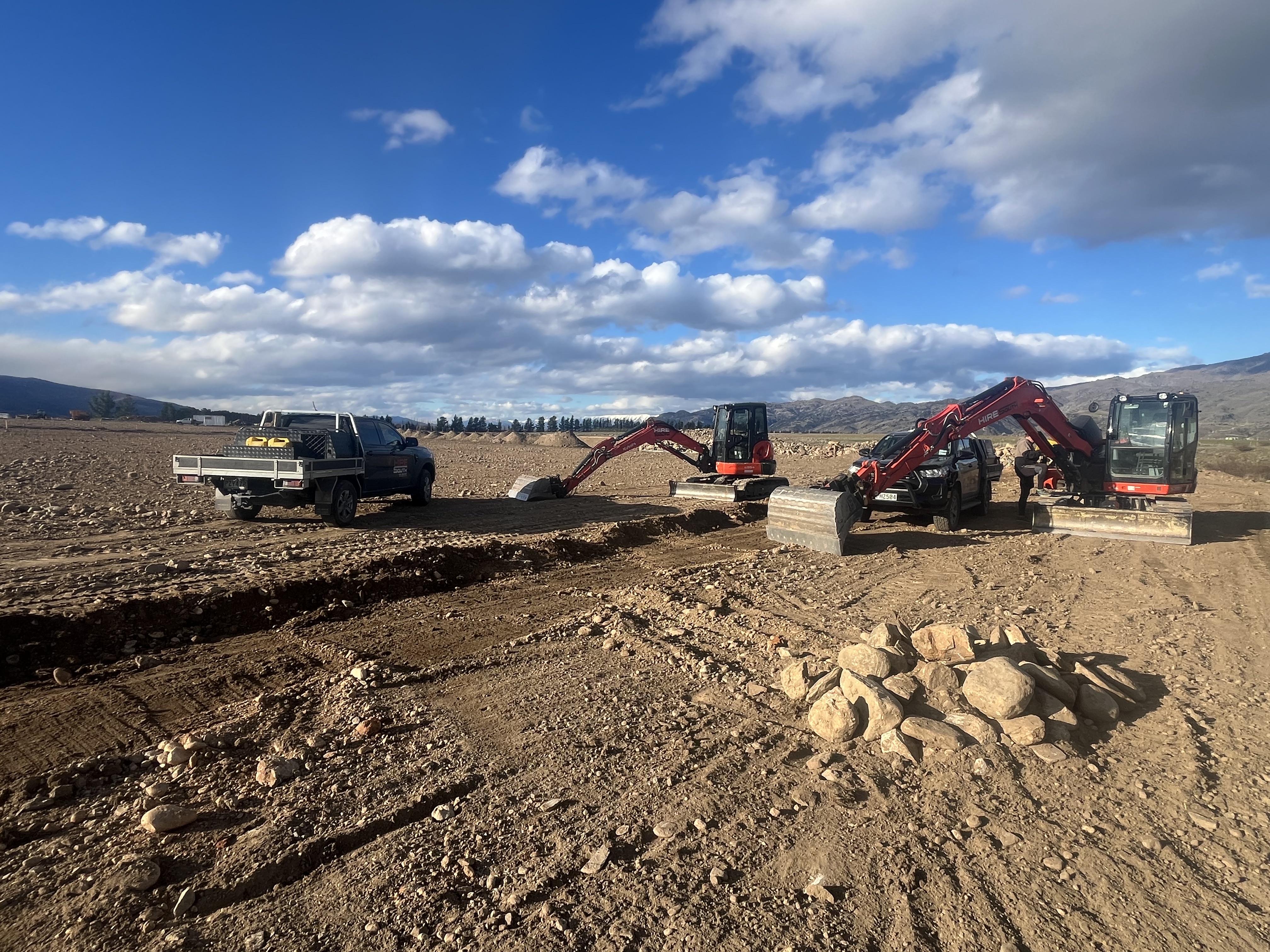 Hire South support ute and two Kubota diggers working on a large open site establishment and earthworks project, Central Otago under a big blue sky with dramatic clouds