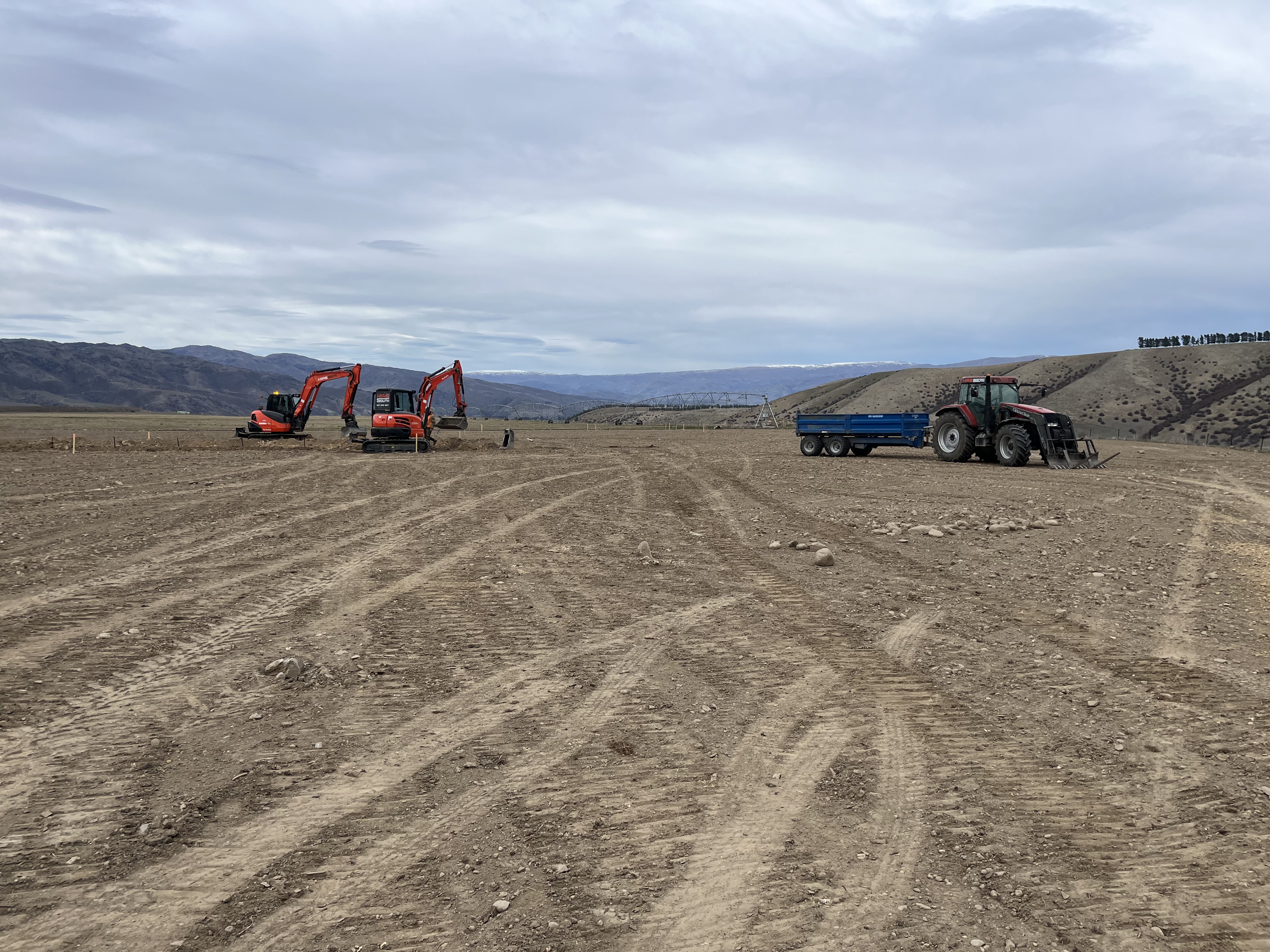 Two Hire South Kubota diggers and a tractor on a large open earthworks site with Central Otago ranges in the background