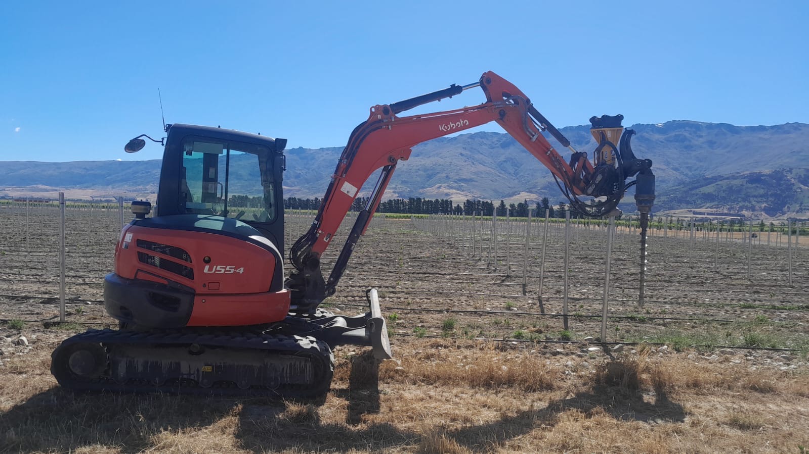 Hire South Kubota U55 digger with post driver attachment working on vineyard posting in Central Otago, clear blue sky