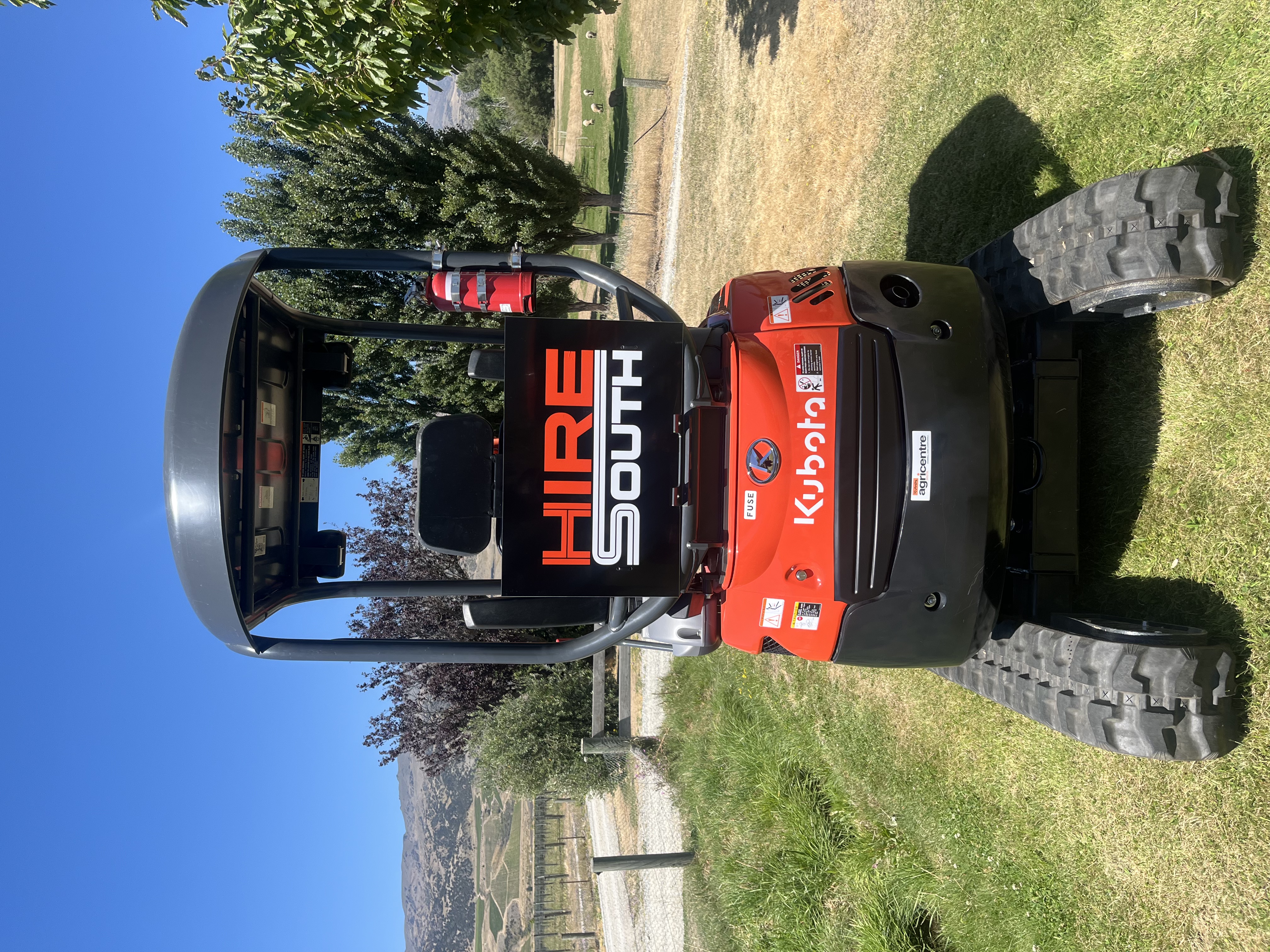 Hire South branded Kubota U17-3 mini digger, side profile with Central Otago landscape in the background
